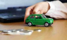 Modellino di auto verde circondata da monete e un laptop